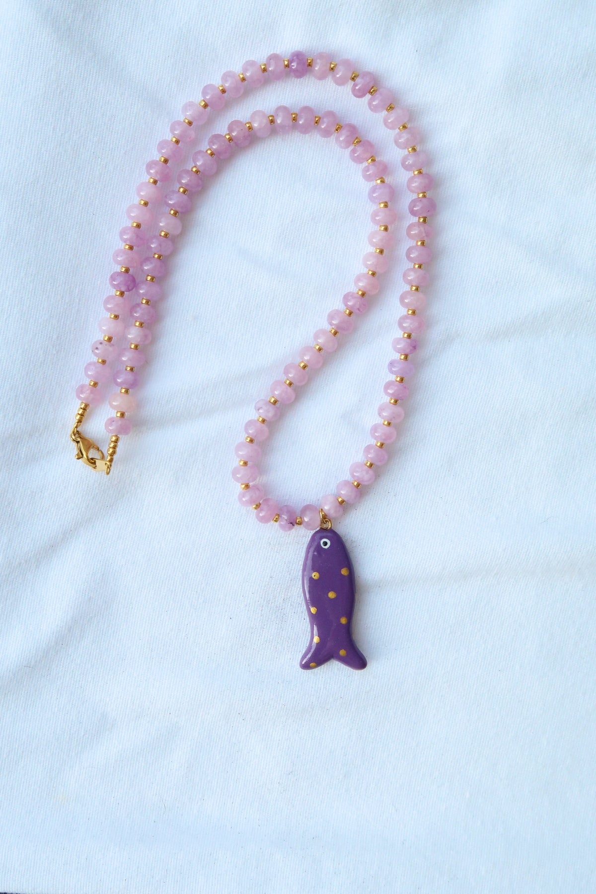 Necklace with a gold-dotted purple fish pendant on a light purple bead chain against a white background