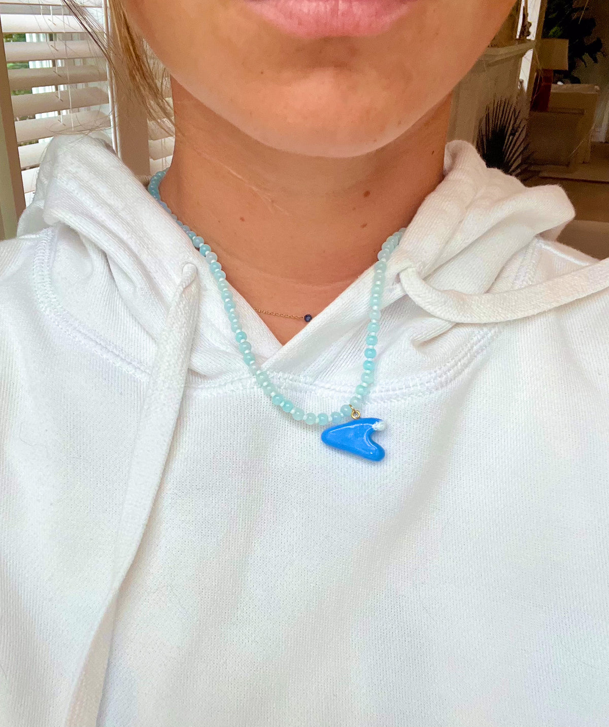 Person wearing a white hoodie with a blue wave pendant necklace