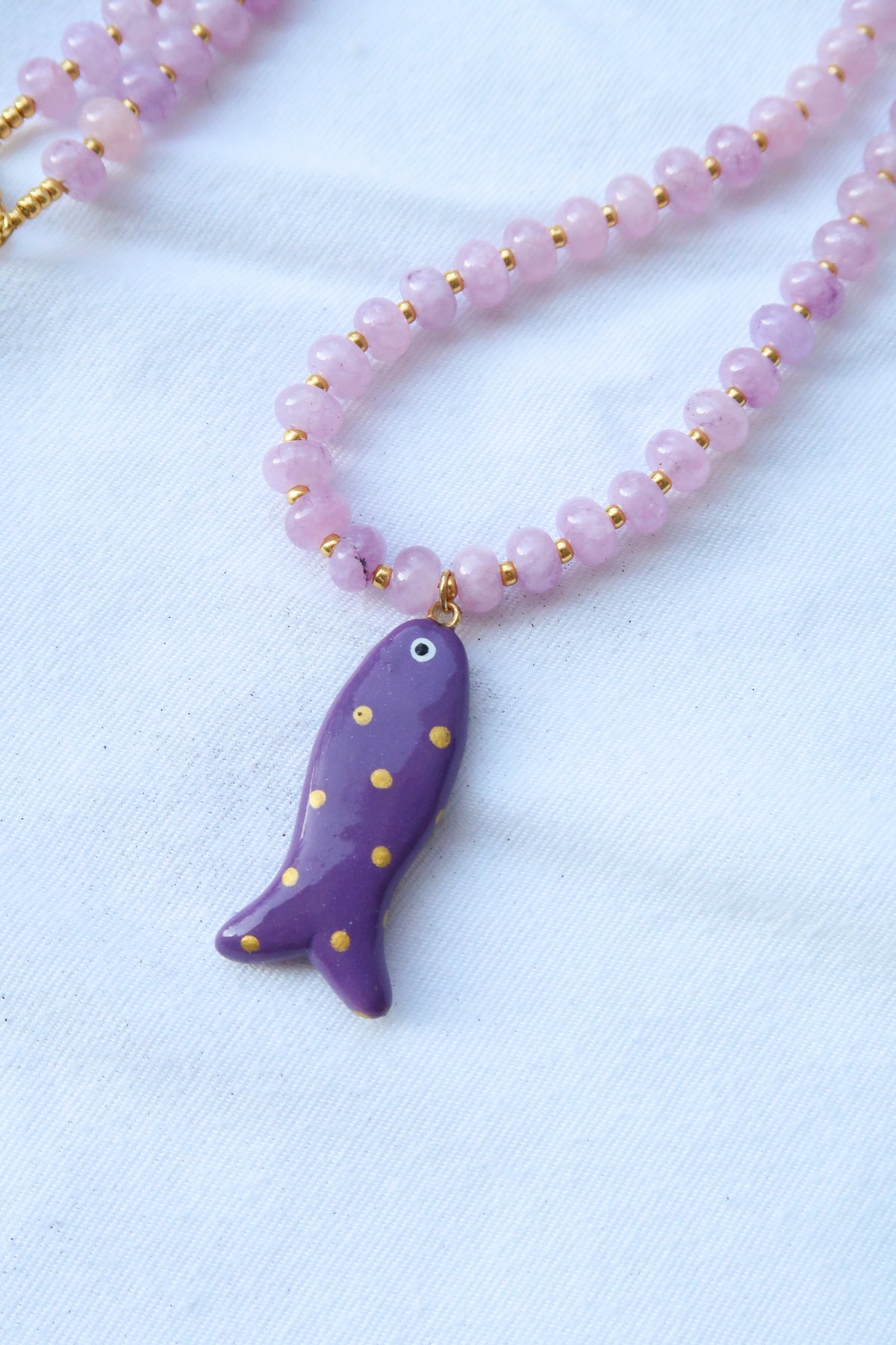Necklace with a gold-dotted purple fish pendant on a light purple bead chain against a white background