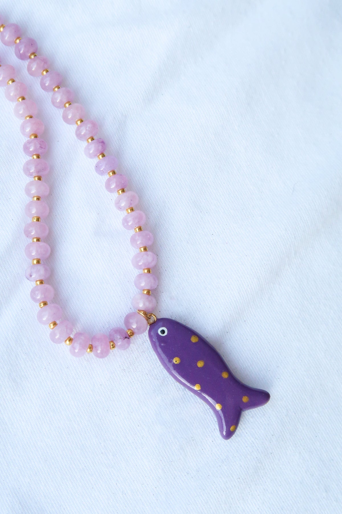 Necklace with a gold-dotted purple fish pendant on a light purple bead chain against a white background