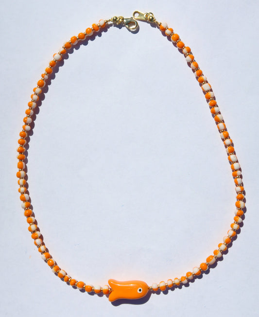 An orange and white beaded necklace with a small orange fish-shaped charm, displayed on a light gray background.