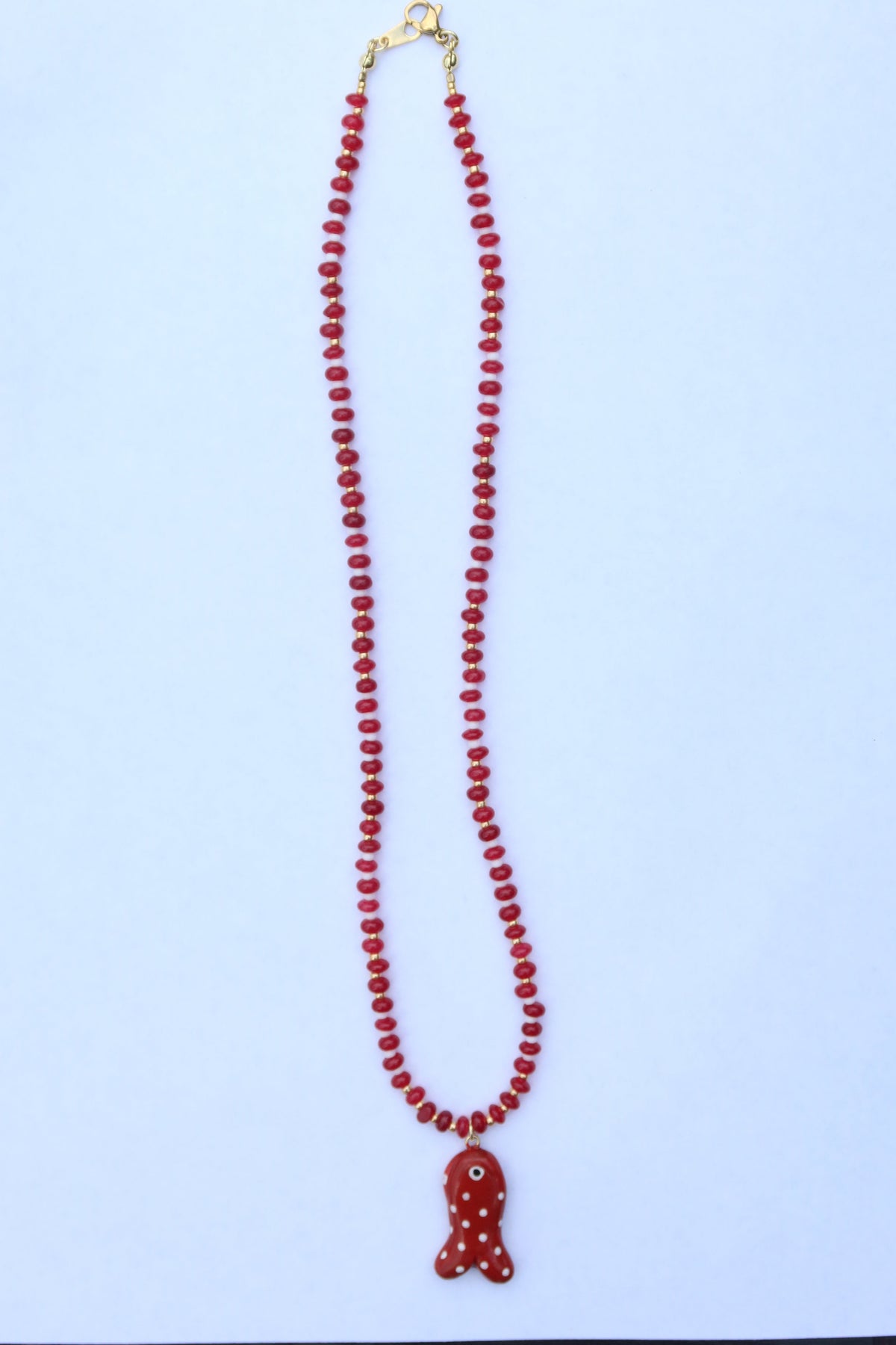 A red beaded necklace with a small red fish-shaped pendant featuring white polka dots, laid out on a light blue background.