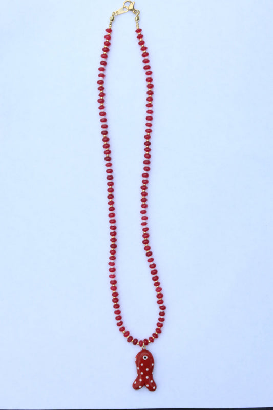 A red beaded necklace with a small red fish-shaped pendant featuring white polka dots, laid out on a light blue background.